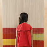 Young child in red organic cotton outfit standing in front of a colorful textile backdrop
