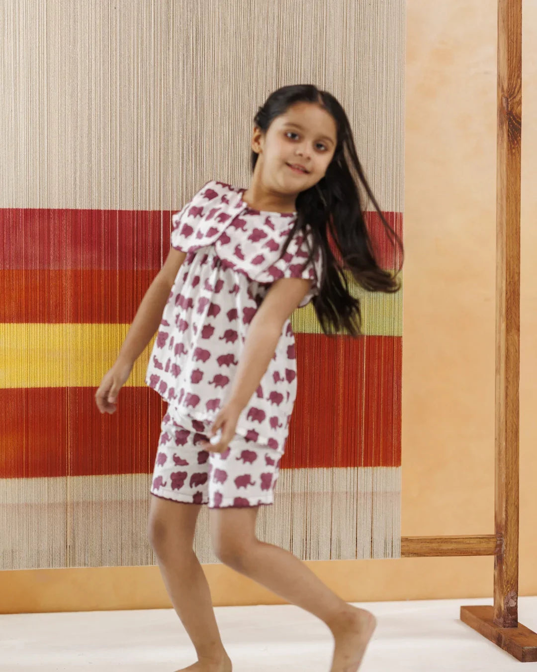 Girl in organic cotton elephant print shorts set, sustainable kidswear, playful setting