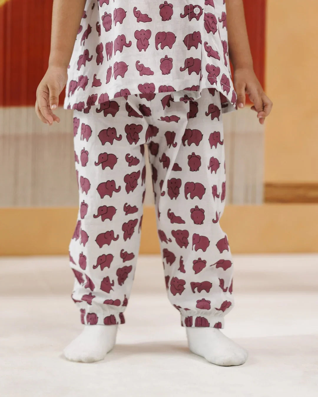 Child wearing white organic cotton pajamas with purple elephant print, standing indoors