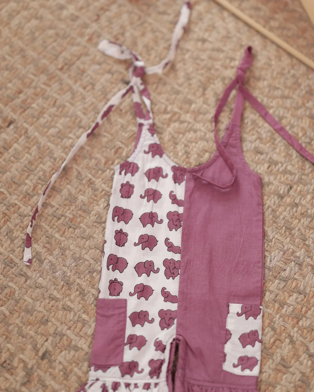 Organic cotton toddler jumpsuit with purple elephant block print and tie straps on woven mat