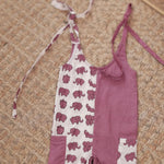 Organic cotton toddler jumpsuit with purple elephant block print and tie straps on woven mat