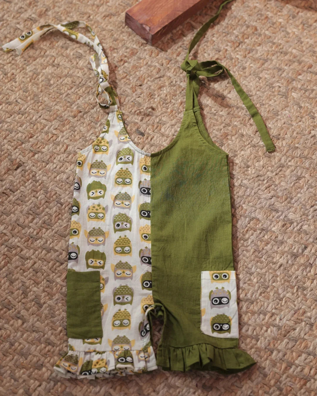 Organic cotton baby romper with green and owl print, ruffle hem, and tie straps on jute rug